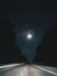 Road amidst illuminated street against sky at night