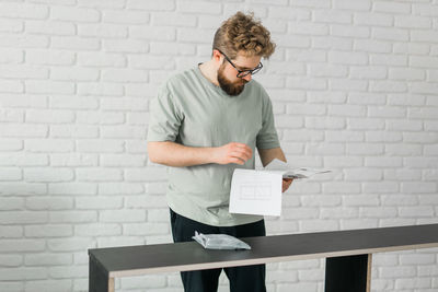 Young man using mobile phone against wall