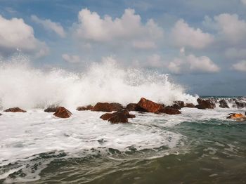 Waves splashing on rocks against sky