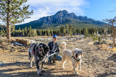 Man kneeling with two dogs in front of a mountain in estes park