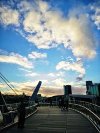 People walking on bridge in city against sky