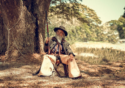 Bearded man with rifle sitting in forest