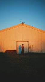 Rear view of woman standing by barn against clear blue sky