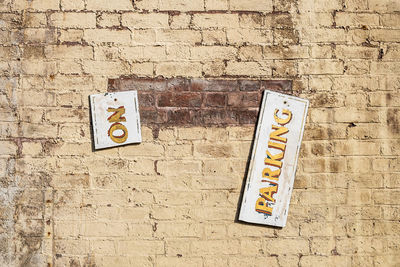 Broken information sign hanging against brick wall