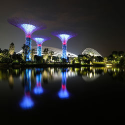 Illuminated city by lake against sky at night