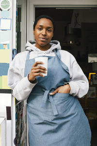 Portrait of shop owner holding disposable cup while standing at entrance