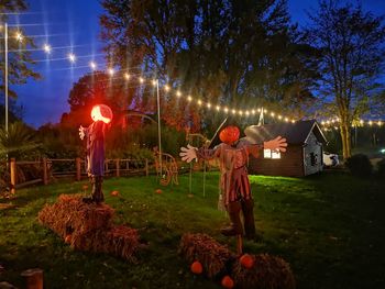 Children standing on field against trees at night