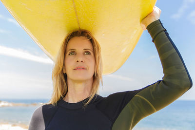 Close-up of woman carrying surfboard on head against sky