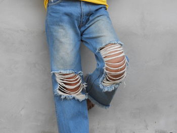 Low section of woman in torn jeans standing against wall