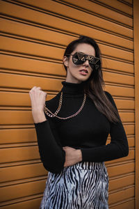 Portrait of young woman wearing sunglasses while standing against wall