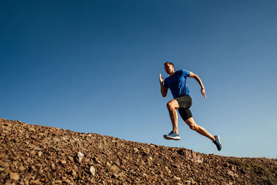 Low angle view of man jumping on rock against clear sky