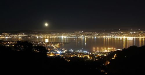 Illuminated cityscape by sea against clear sky at night