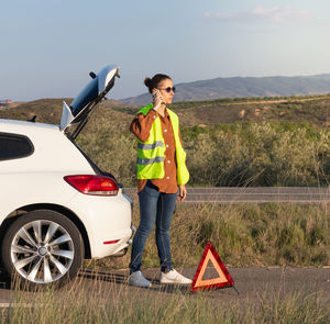 Young man on a vest calling roadside assistance on the smartphone to get the car a fixed