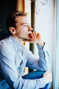 Side view of thoughtful man standing by window at home