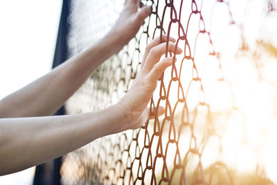 Cropped image of hands holding chainlink fence