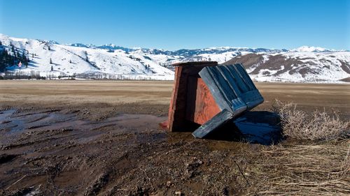 Abandoned hut on field against snowcapped mountains during winter