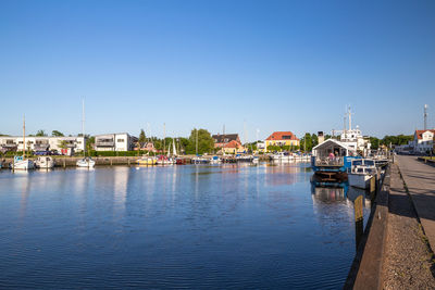 Sailboats moored in river by buildings against clear blue sky