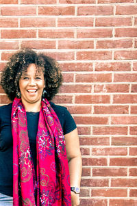 Portrait of smiling mid adult woman standing against brick wall