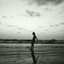 Side view of silhouette boy standing on shore at beach against sky