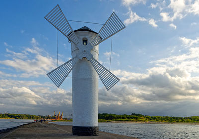 Traditional windmill by sea against sky