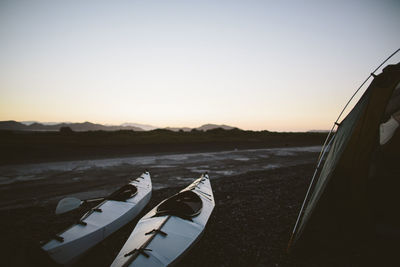 Kayaks on land by tent against clear sky