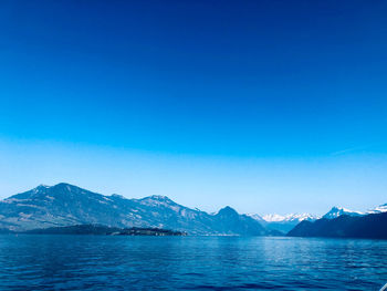 Scenic view of sea and mountains against clear blue sky