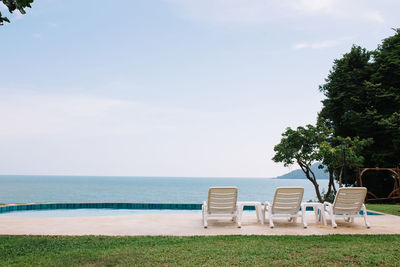 Chairs by swimming pool on beach against sky