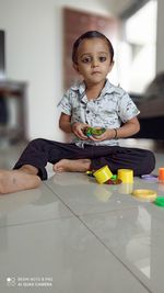 Portrait of cute boy with toy sitting on floor at home