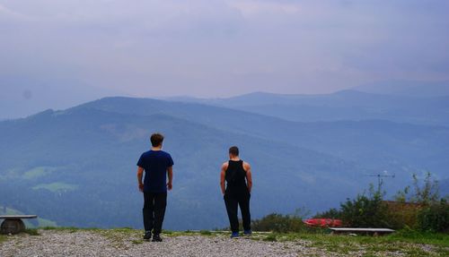 Rear view of men standing on mountain against sky