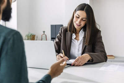 Smiling recruiter interviewing candidate and writing in diary at desk