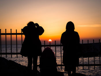 Silhouette people photographing sea against sky during sunset