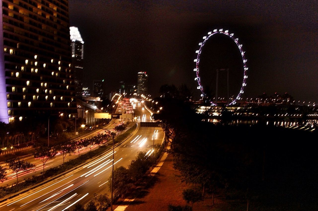 LIGHT TRAILS ON ROAD AGAINST ILLUMINATED BUILDINGS IN CITY