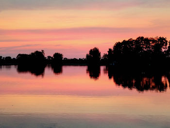 Silhouette trees by lake against romantic sky at sunset