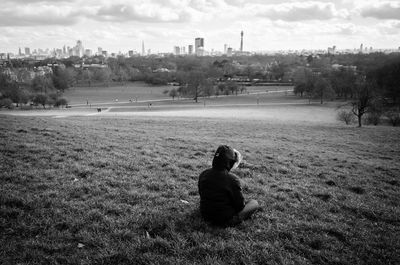 Rear view of man sitting on field against sky