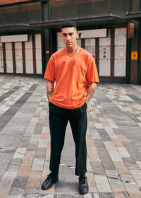 Portrait of young man standing on footpath against building