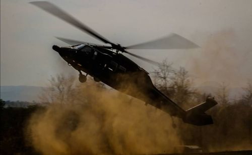 Helicopter flying over field against sky