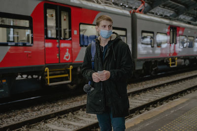 A young boy in a medical mask, with tickets in his hands, against the background of a train, stands 