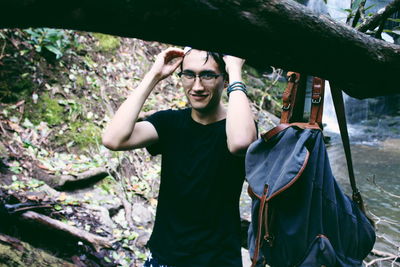 Portrait of young man wearing eyeglasses standing against waterfall