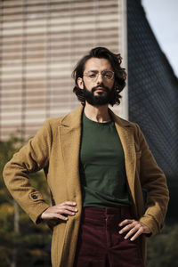 Confident man with hands on hip in front of building