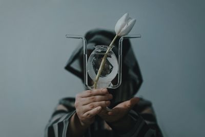 Person wearing raincoat while holding tulip against gray background