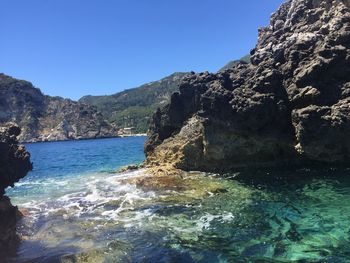 Scenic view of sea by mountains against clear blue sky