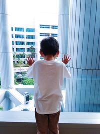 Rear view of boy looking through window