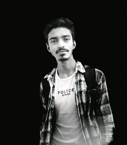 Portrait of young man standing against black background