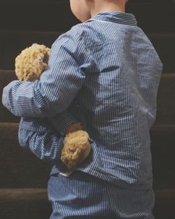 Rear view of boy holding teddy bear against staircase