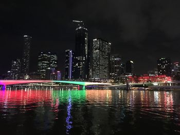 Illuminated buildings by river against sky at night