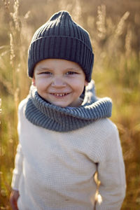 Boy in warm clothes stand on chair along a path on a field with dried grass in autumn