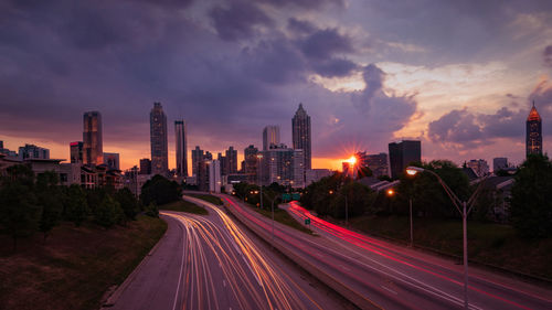 Light trails on road amidst buildings in city against sky