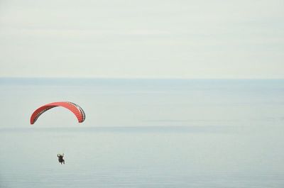 Person paragliding over seascape against sky