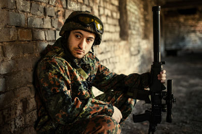 Young soldiers with guns, a soldier in equipment and with arms inspects a ruined house outside the