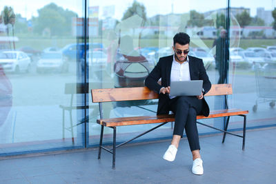 Businessman using digital tablet while sitting on bench outdoors